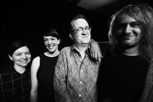 Black-and-white photo of bearded man, spectacled man wearing patterned shirt, two dark-haired women